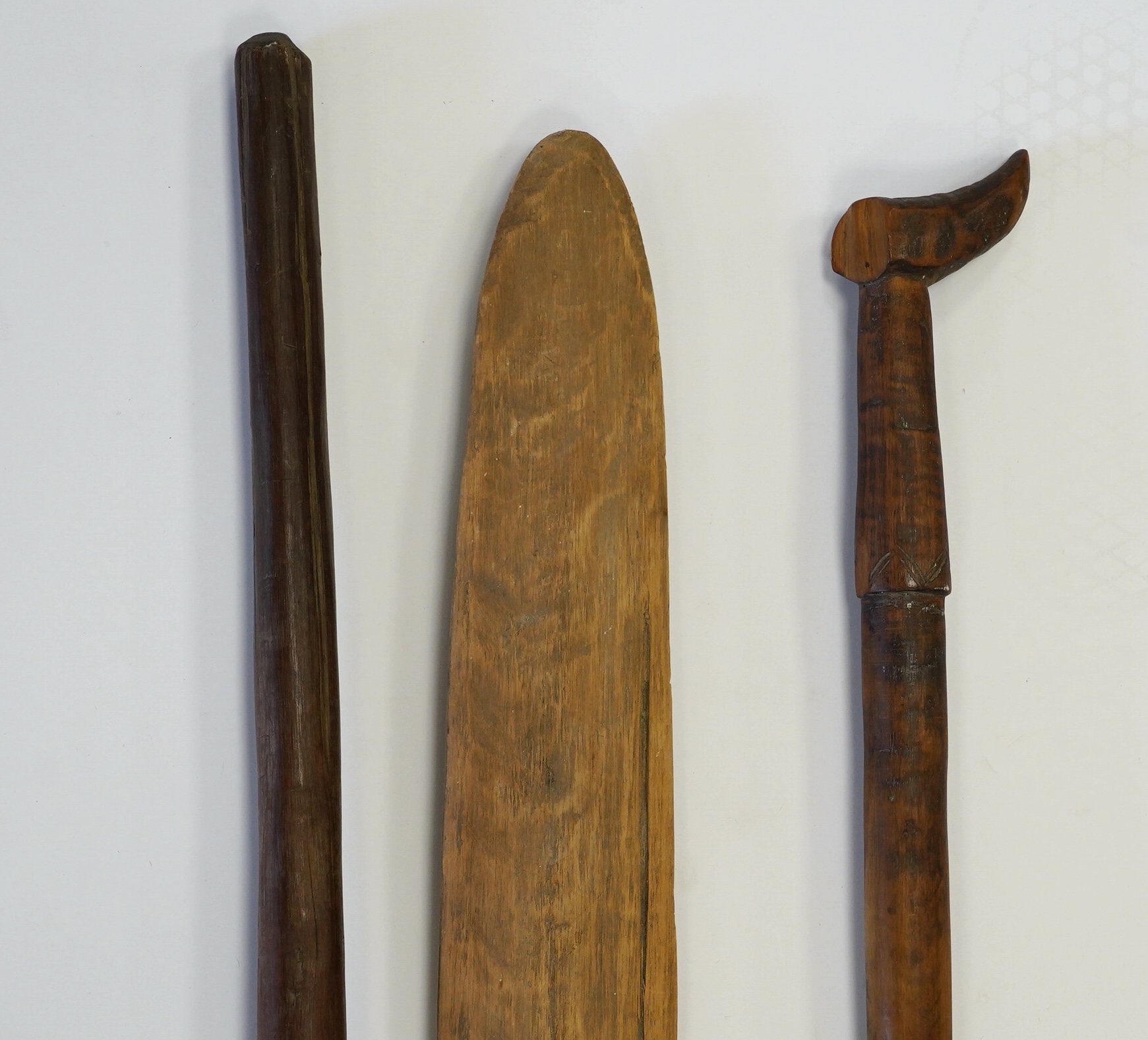 Two tribal carved wood paddles and an ironwood club, longest 104cm. Condition - poor to fair, one paddle missing part of the grip, splits to the wood, etc.